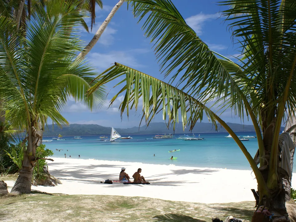 A tropical beach scene with palm trees, white sand, and lounge chairs.