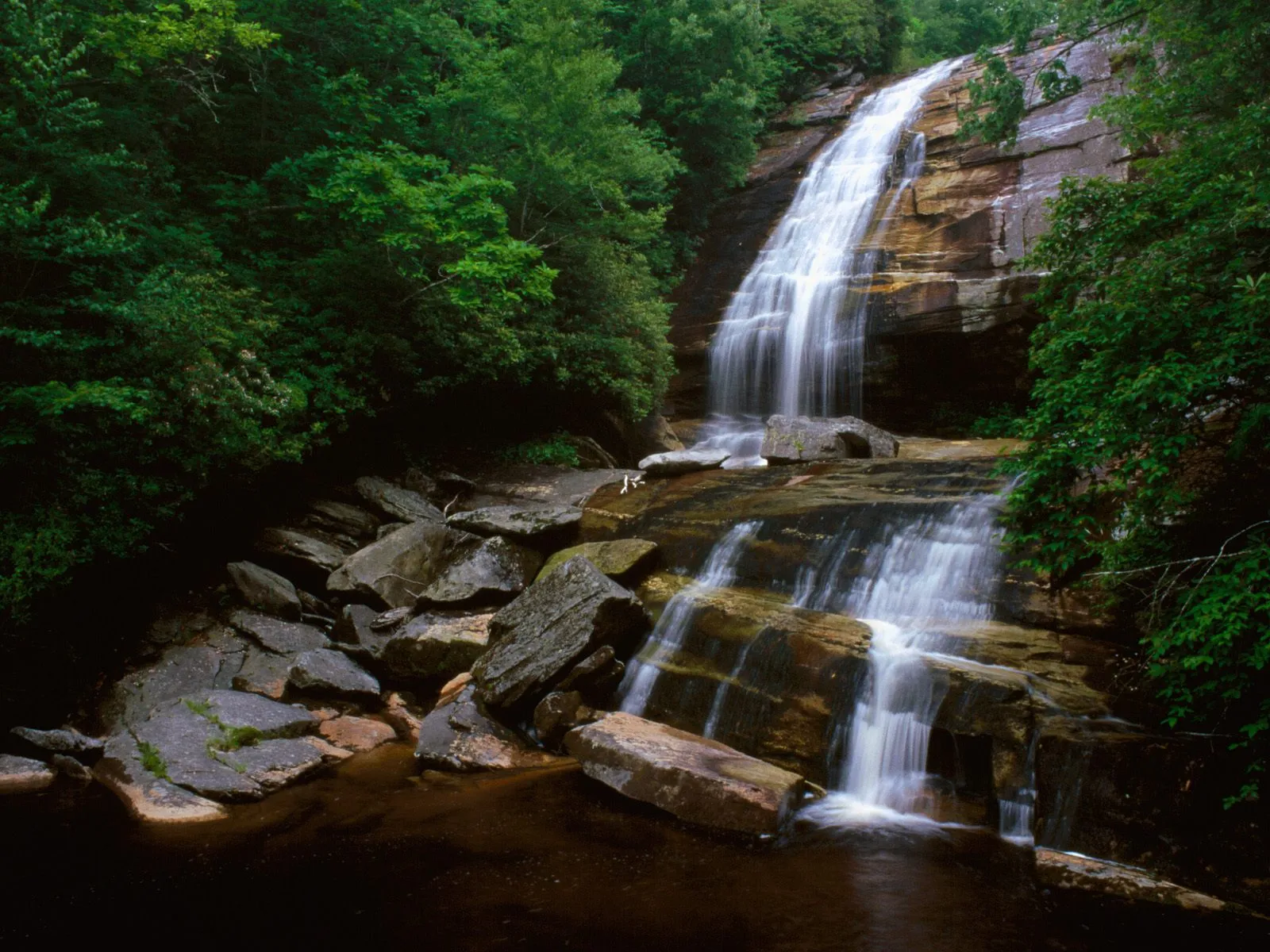A serene waterfall cascades down rock ledges with smooth, silky water.