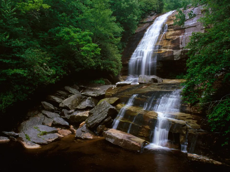 A serene waterfall cascades down rock ledges with smooth, silky water.