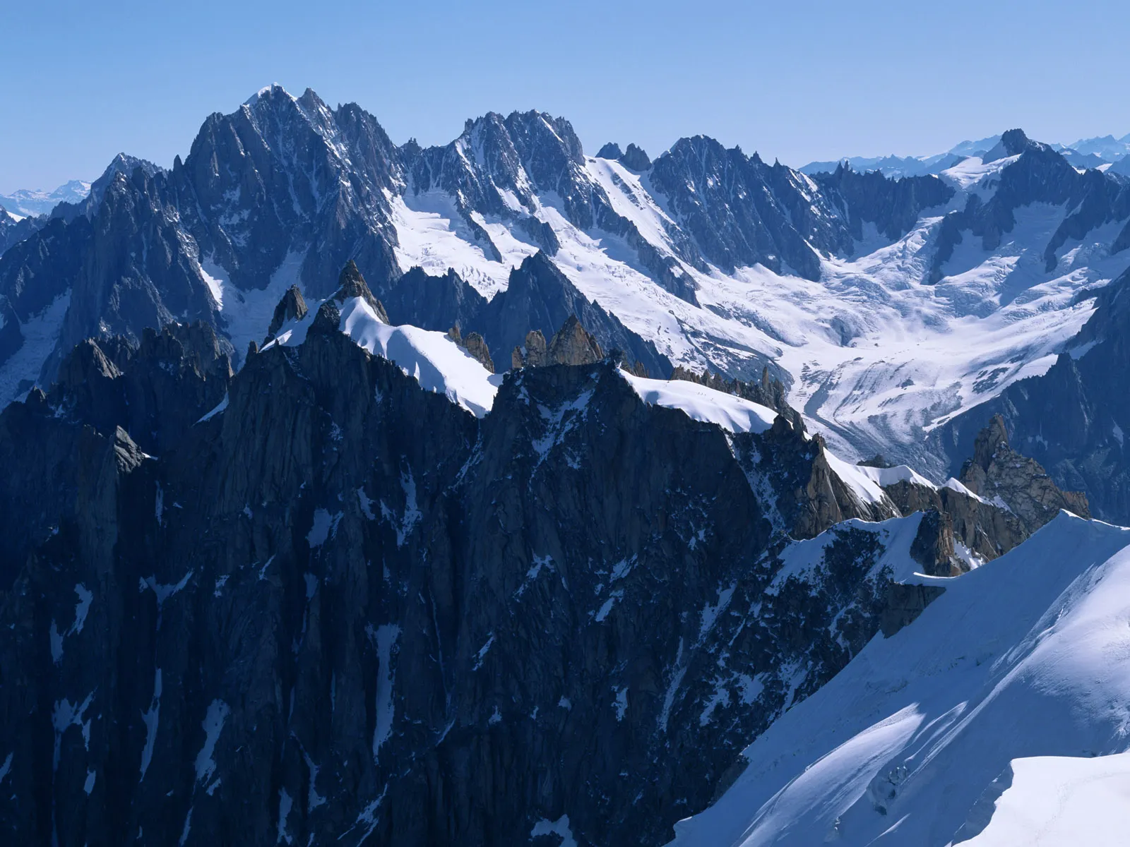 Sharp, rocky mountain peaks partially covered in snow and ice under a clear blue sky.