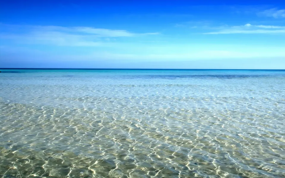 Sunlight creates shimmering patterns on the sandy seabed through clear, shallow tropical waters.