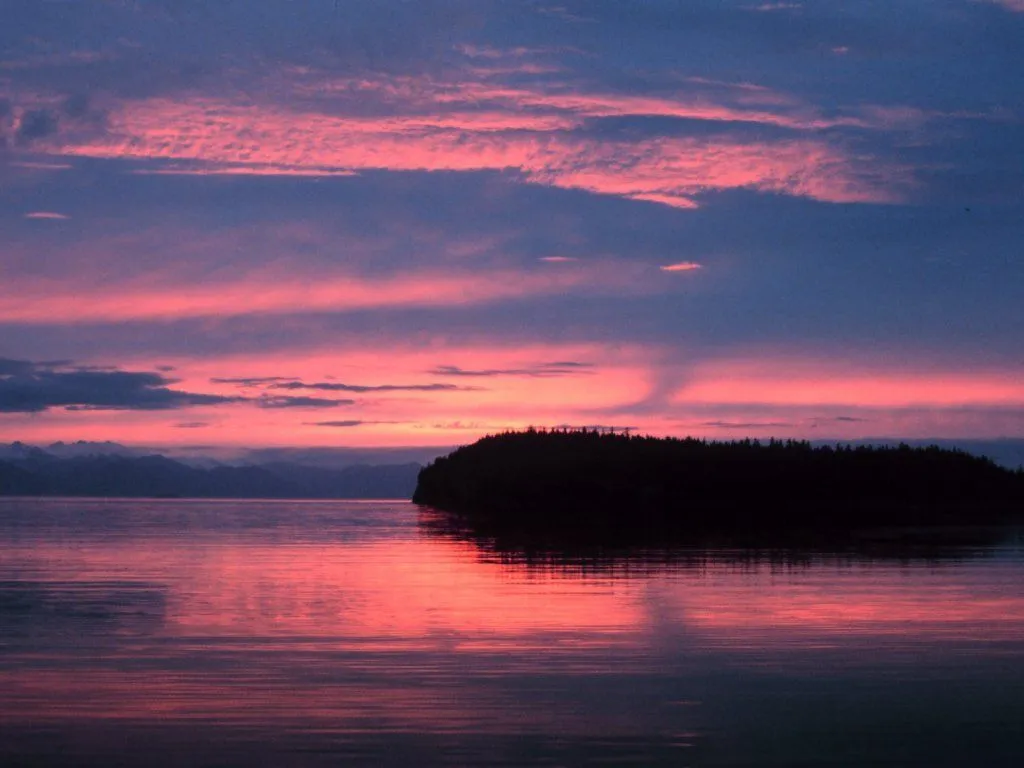 A dark, silhouetted island juts into the water under a pink and purple sunset sky.