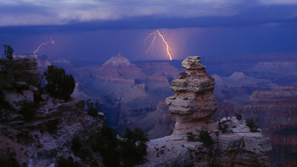 A single, powerful lightning bolt illuminates the Grand Canyon at dusk.