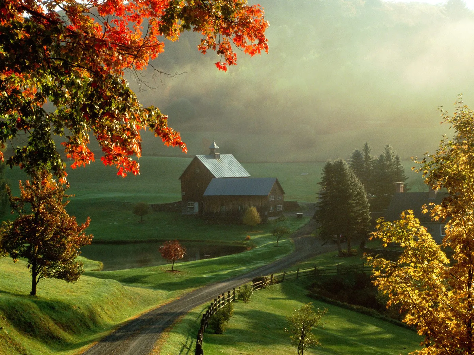 A rustic barn and farmhouse nestled in a misty valley during autumn, with vibrant fall foliage.