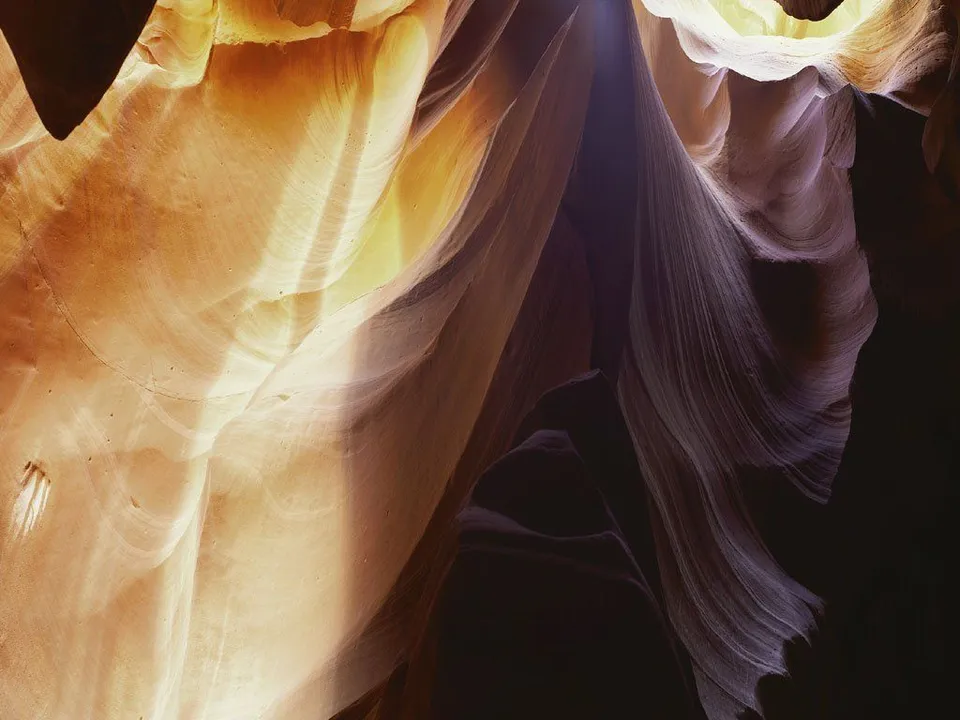 Sunlight streams down into a narrow slot canyon, illuminating the smooth, undulating sandstone walls.