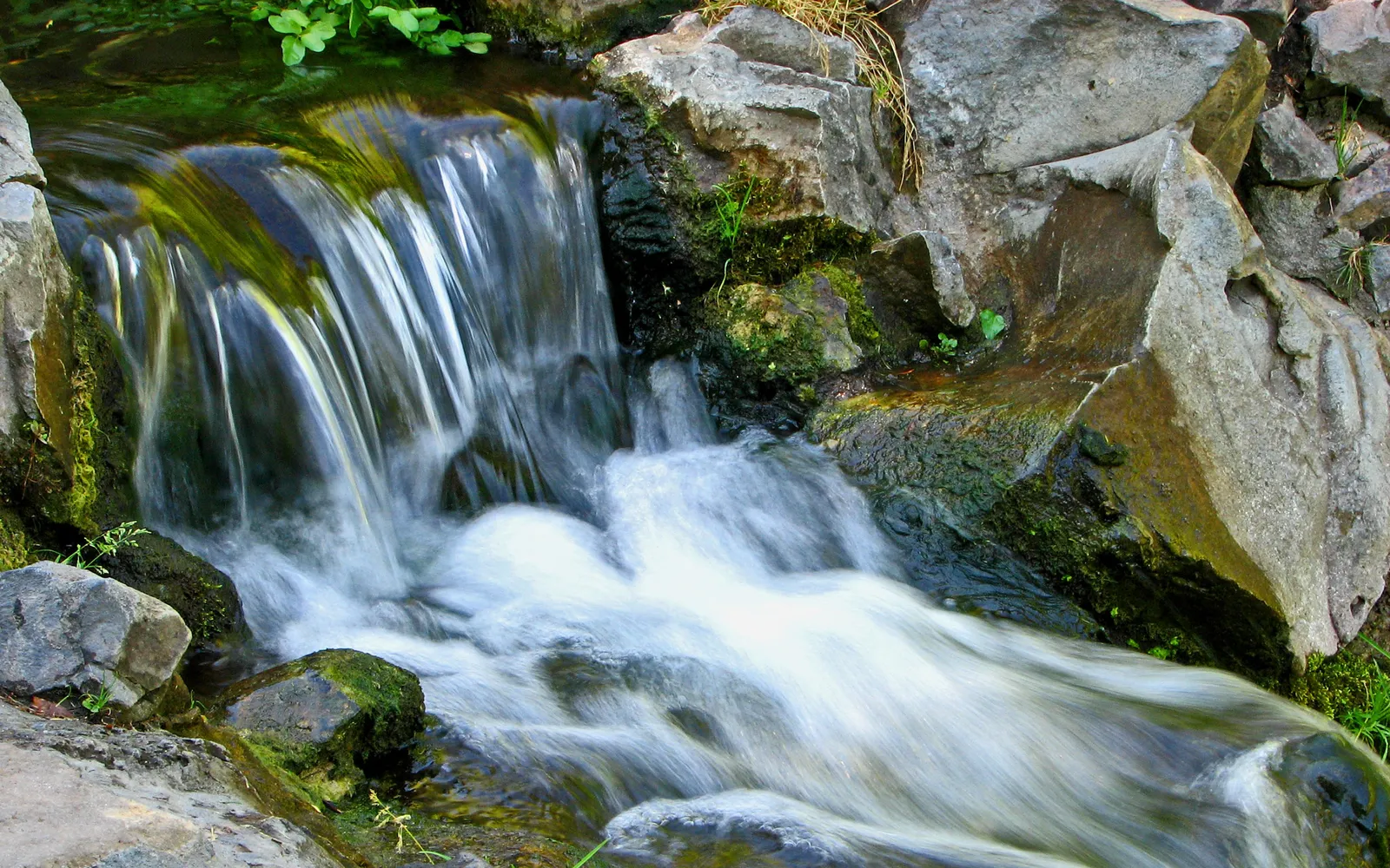 A small waterfall cascades over moss-covered rocks, with smooth, blurred water.