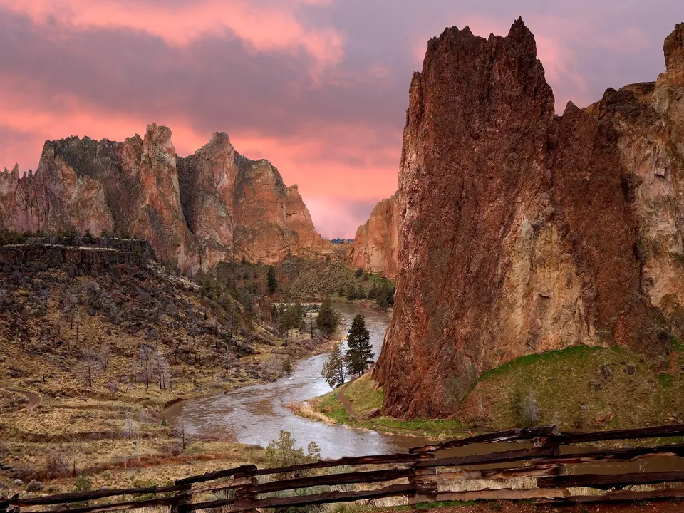 A winding river flows through a canyon with towering rock formations under a vibrant pink and orange sunset sky.