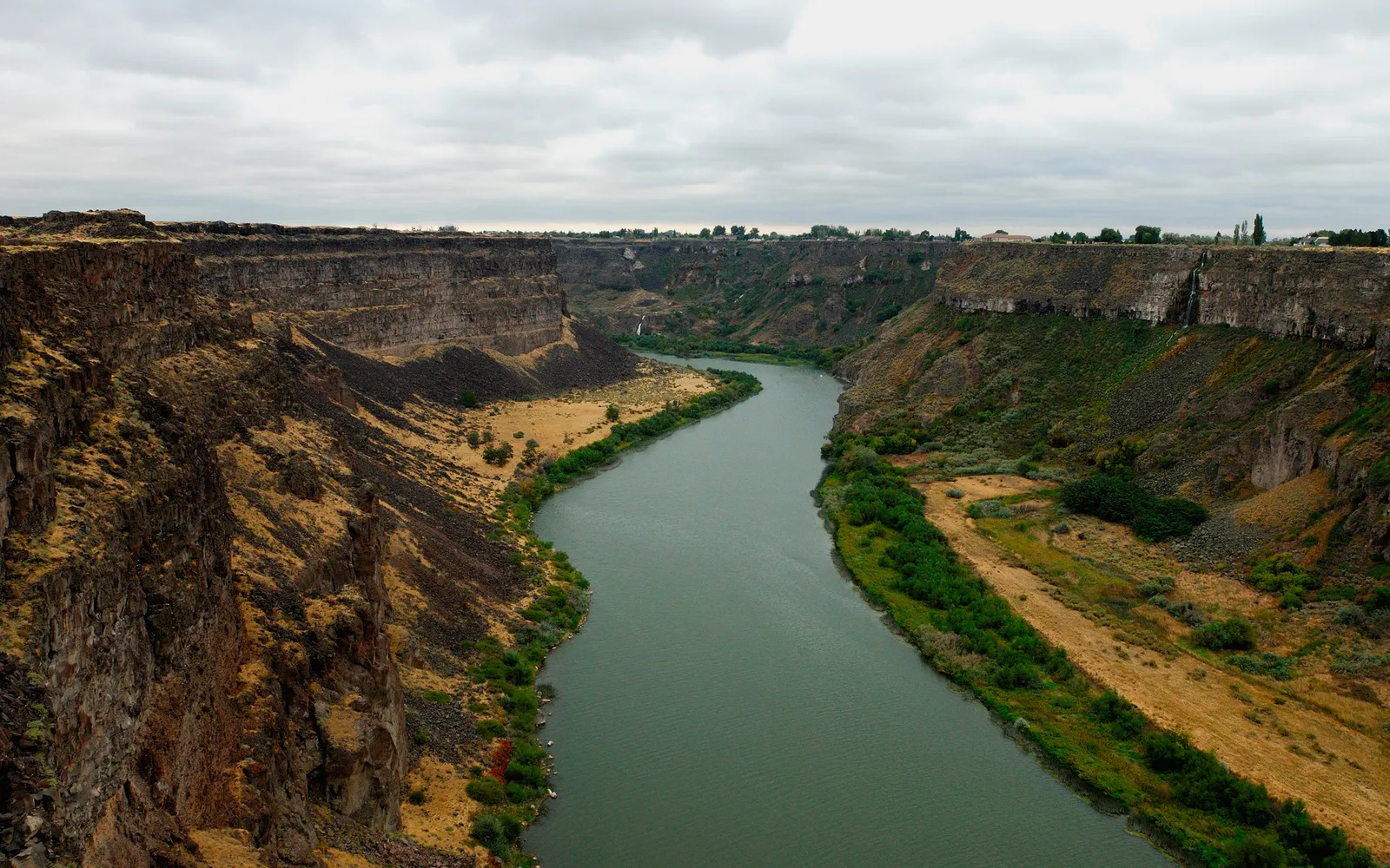 A wide, green river flows through a deep canyon with steep, rocky walls and sparse vegetation.