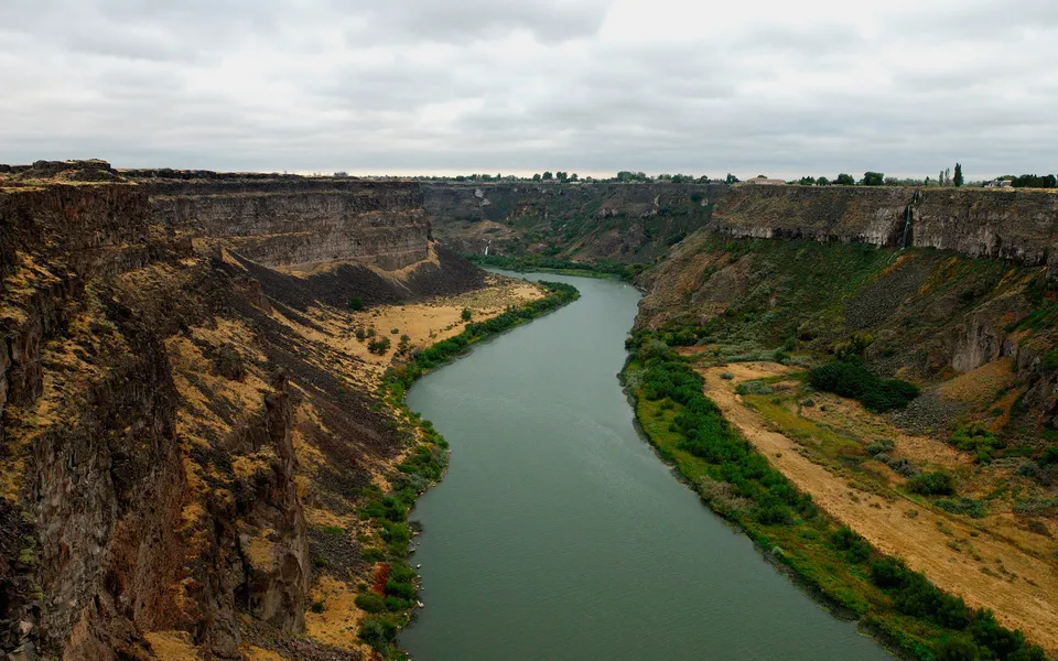 A wide, green river flows through a deep canyon with steep, rocky walls and sparse vegetation.
