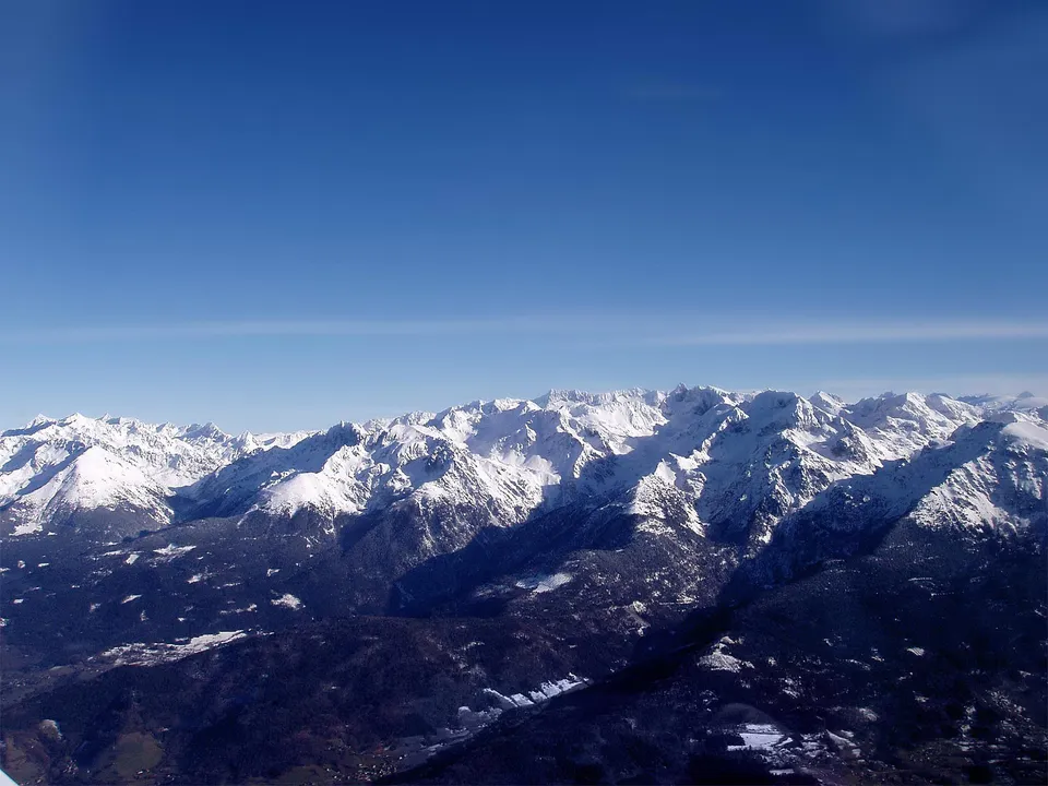 Rugged snow-covered mountains under a clear blue sky, with deep shadows highlighting the terrain.