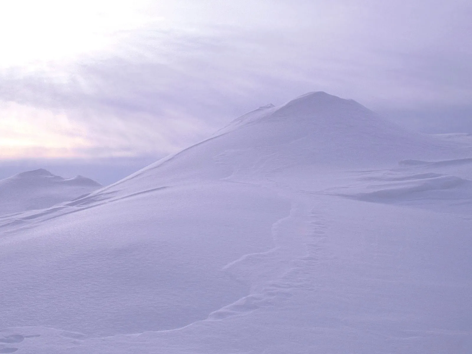 Rolling snow-covered hills under a soft, pastel sky with wispy clouds.