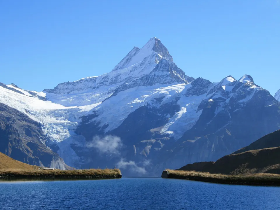 A majestic snow-capped mountain peak dominates the background, with a calm blue lake in the foreground.