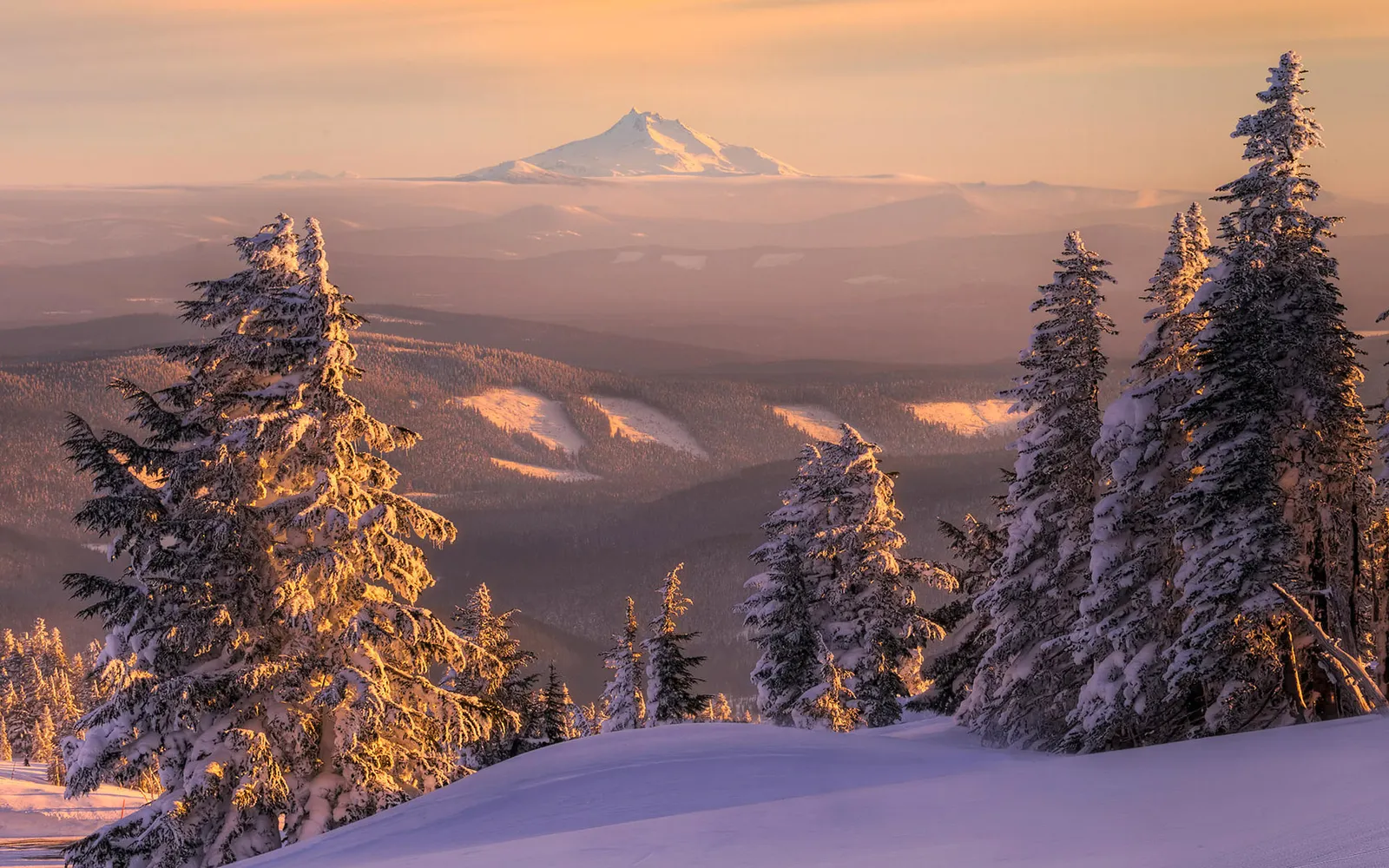 A majestic snow-covered mountain range is bathed in the warm glow of golden hour light.