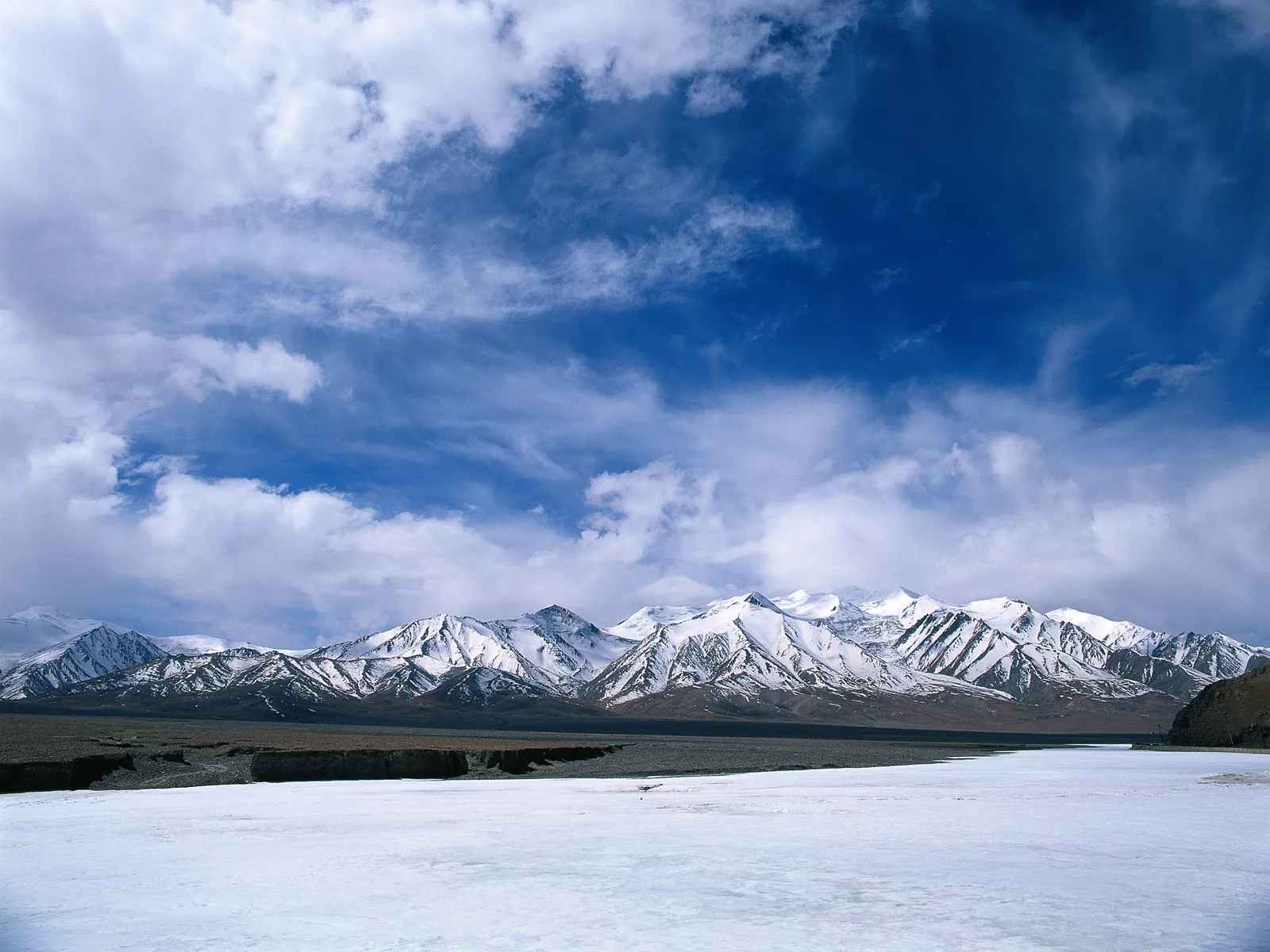 A vast, snow-covered mountain range stretches across the horizon under a dramatic sky with white clouds.