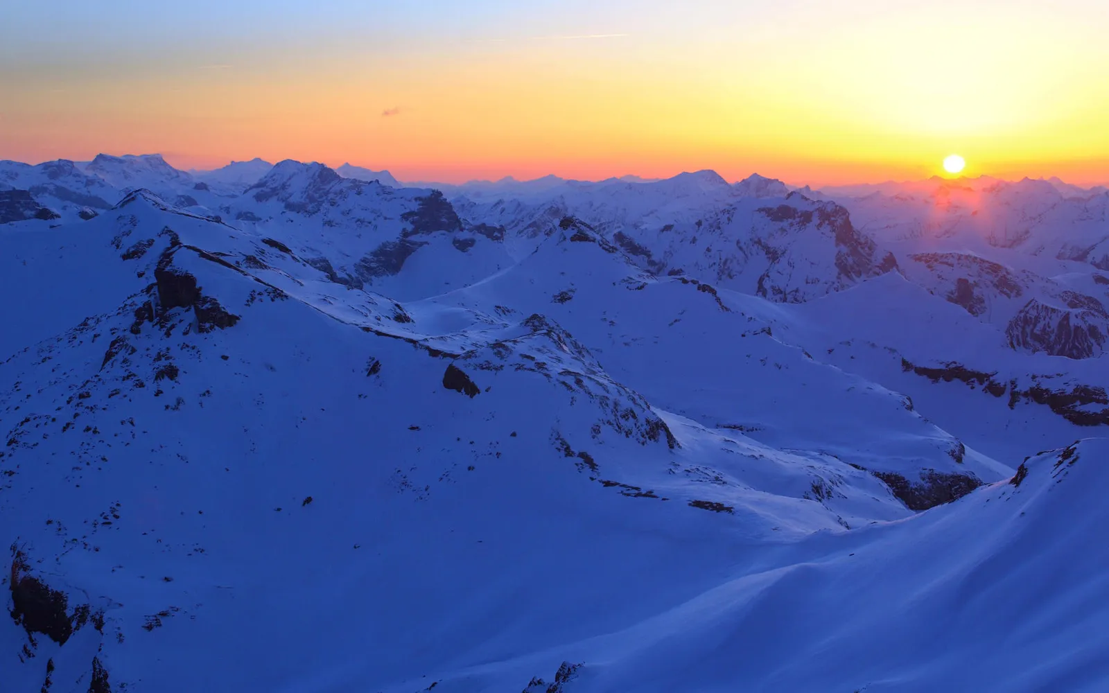 A vast expanse of snow-covered mountains under a vibrant sunset sky.