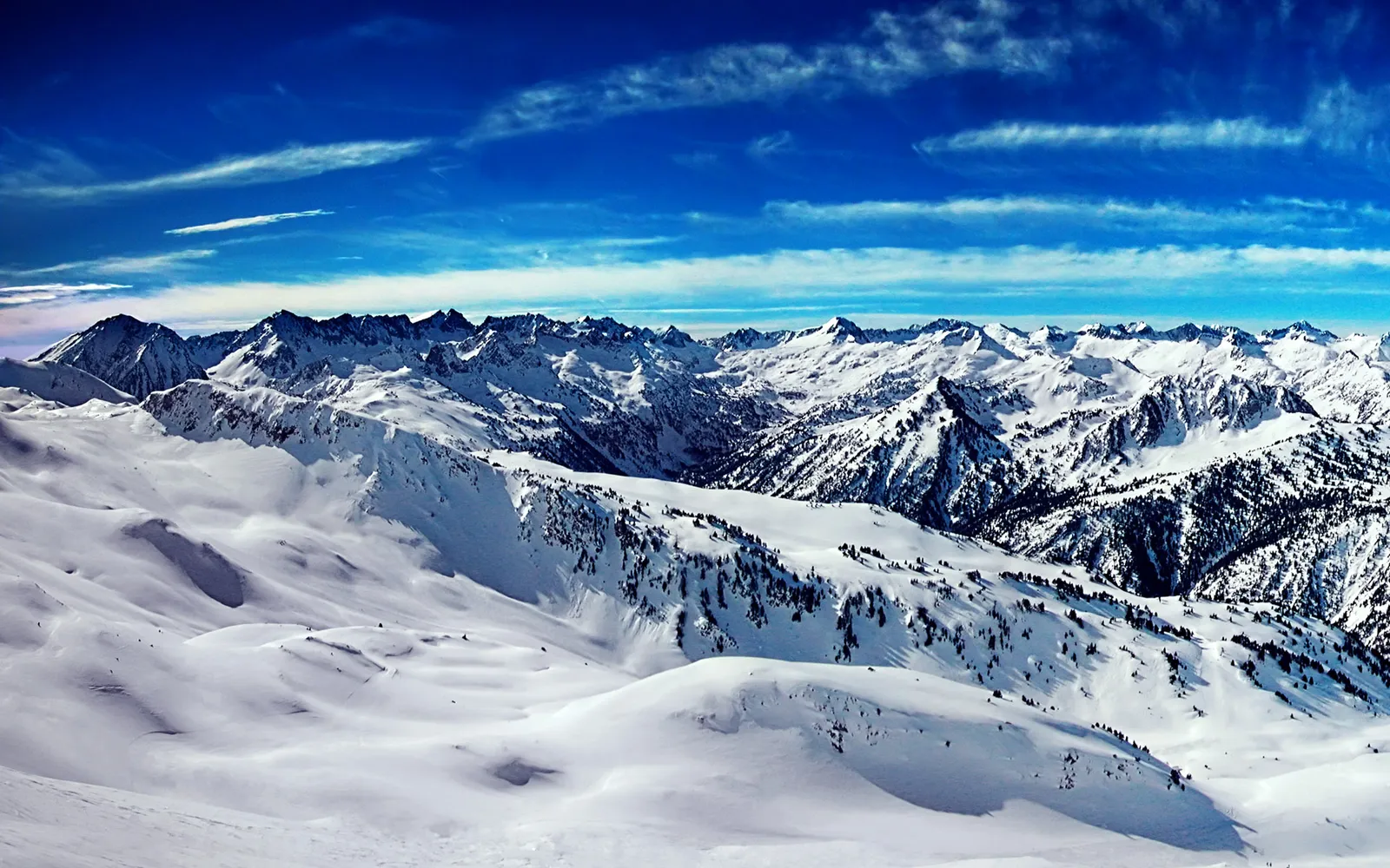 A vast snow-covered mountain range stretches under a vibrant blue sky with thin, wispy clouds.