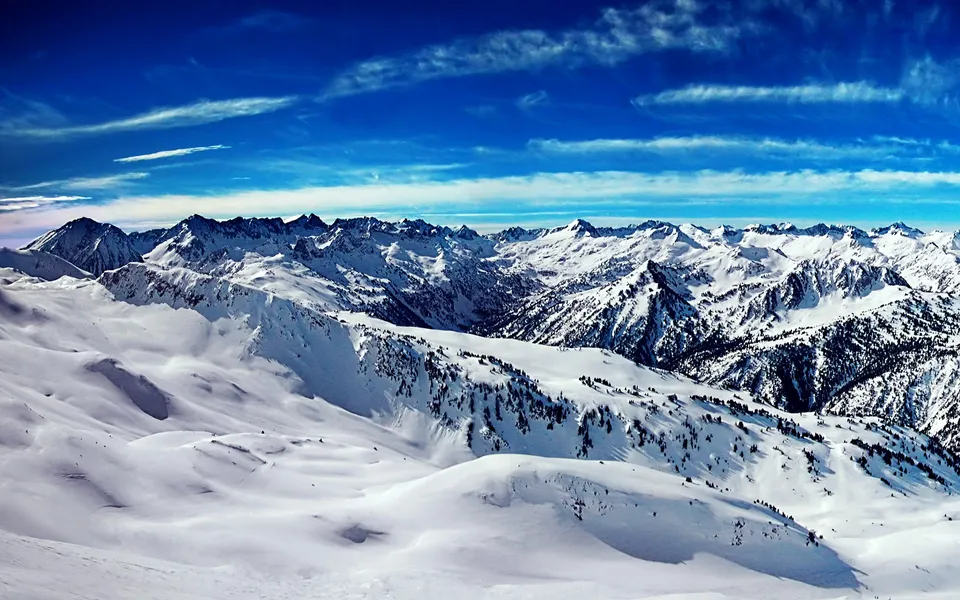 A vast snow-covered mountain range stretches under a vibrant blue sky with thin, wispy clouds.