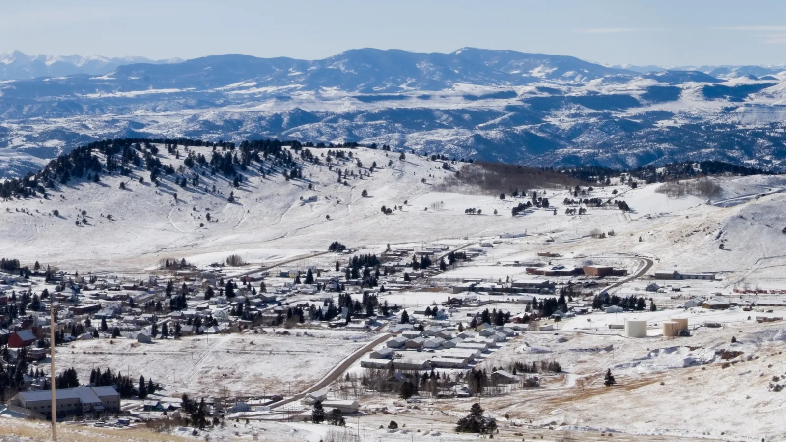 A wide aerial view of a small town nestled in a snow-covered valley, with mountains in the background.