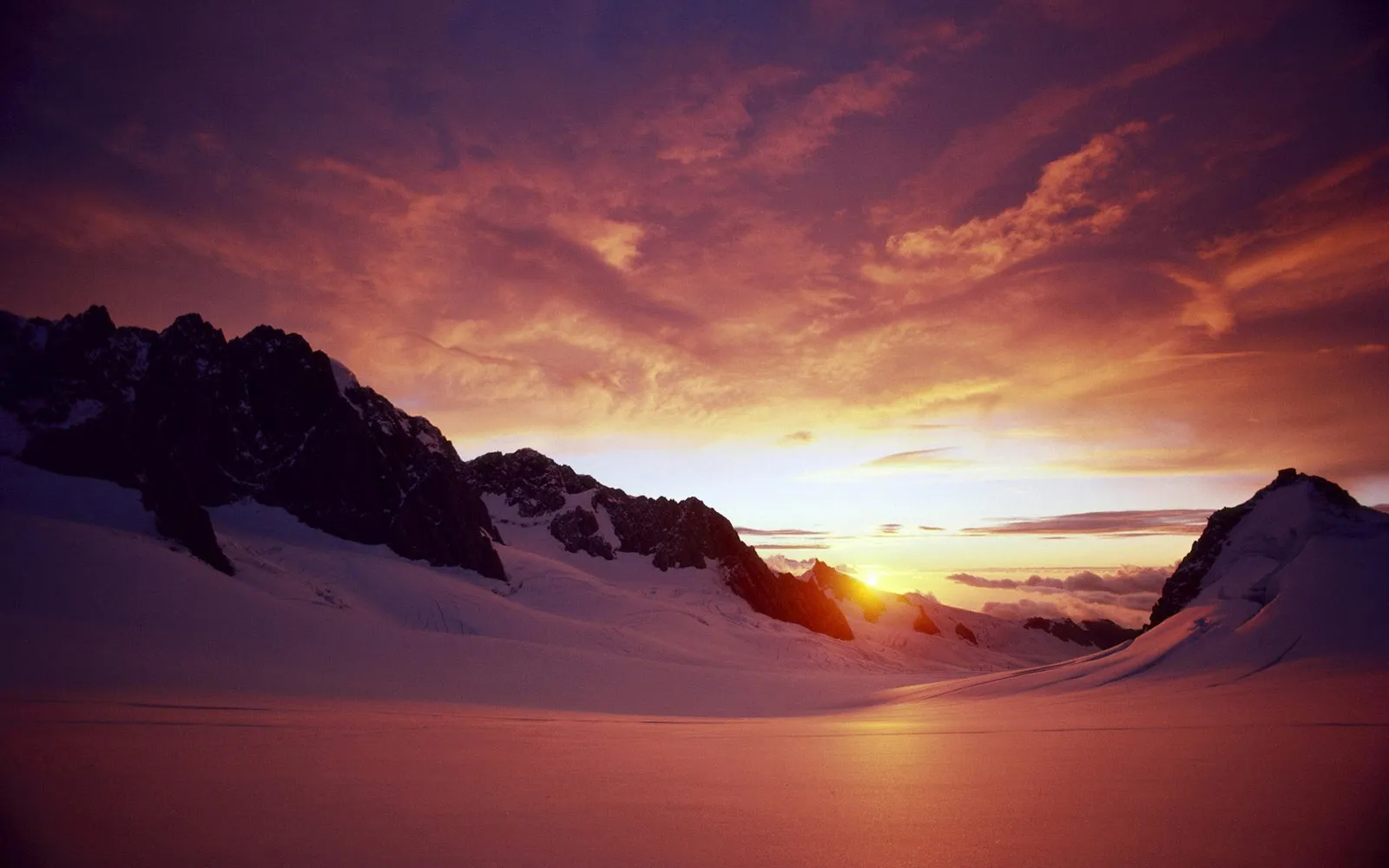 Snow-covered mountains under a vibrant pink and orange sunrise sky.
