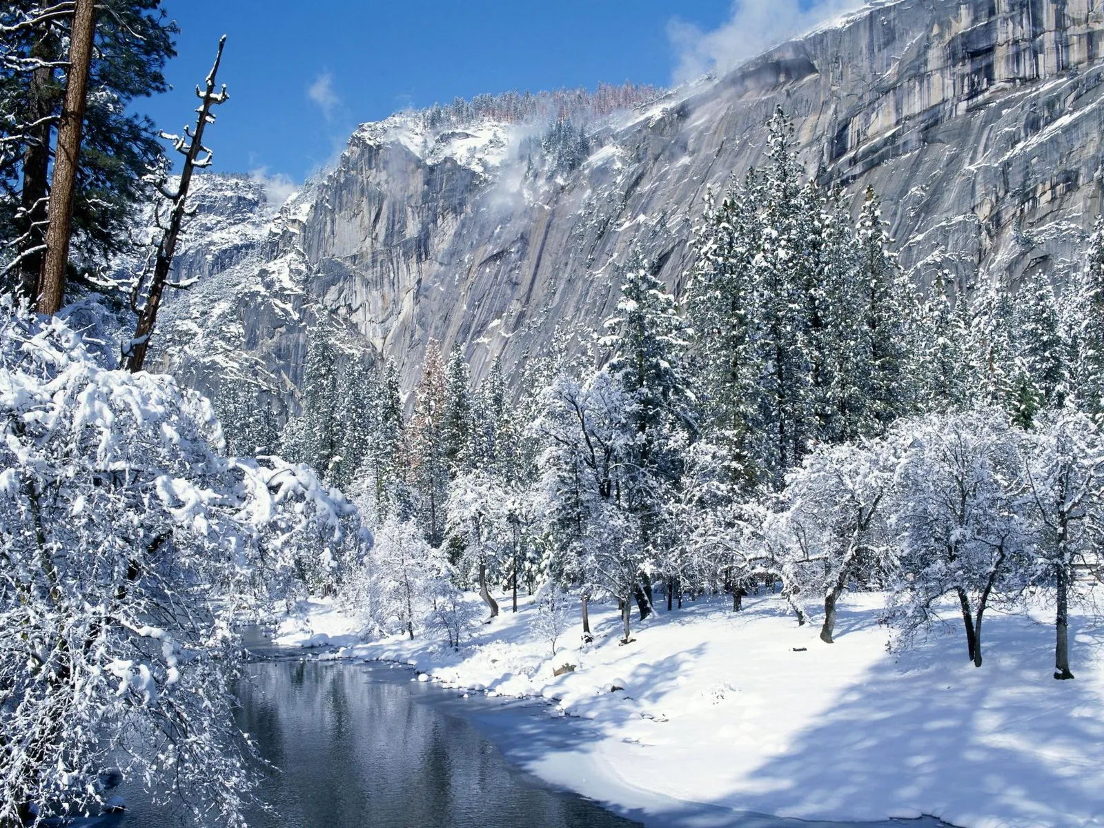 A serene winter scene with a snow-covered valley, a winding river, and a towering granite cliff face.