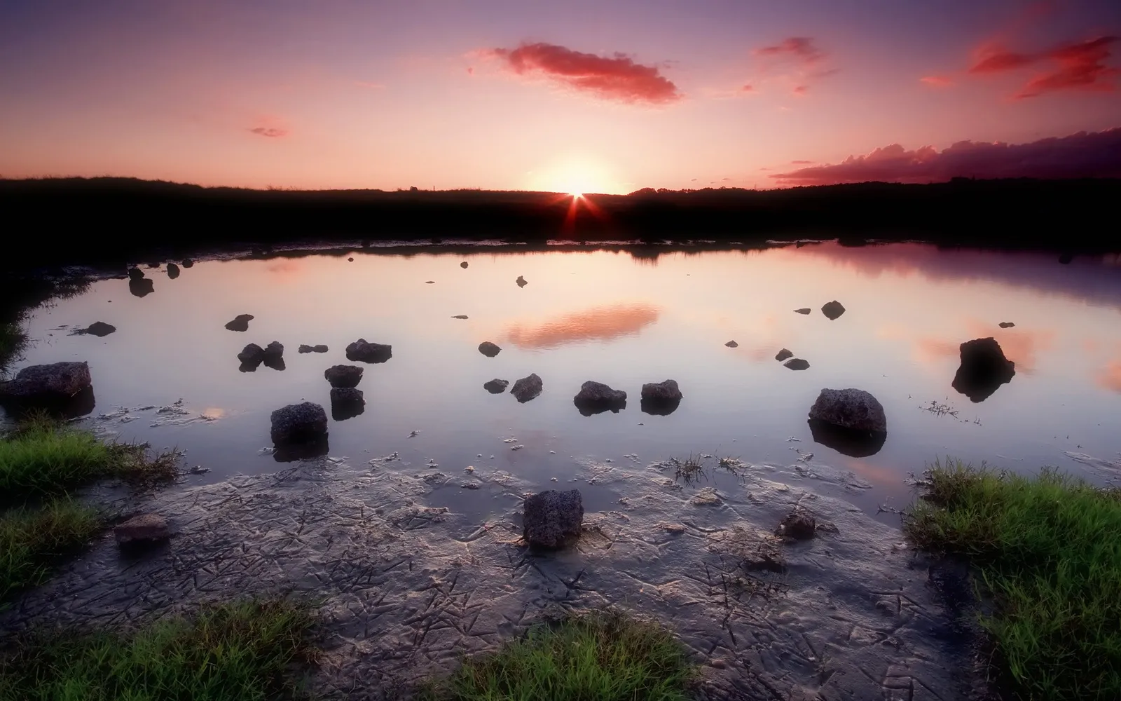 A soft pink and purple sunset over still water with scattered rocks.