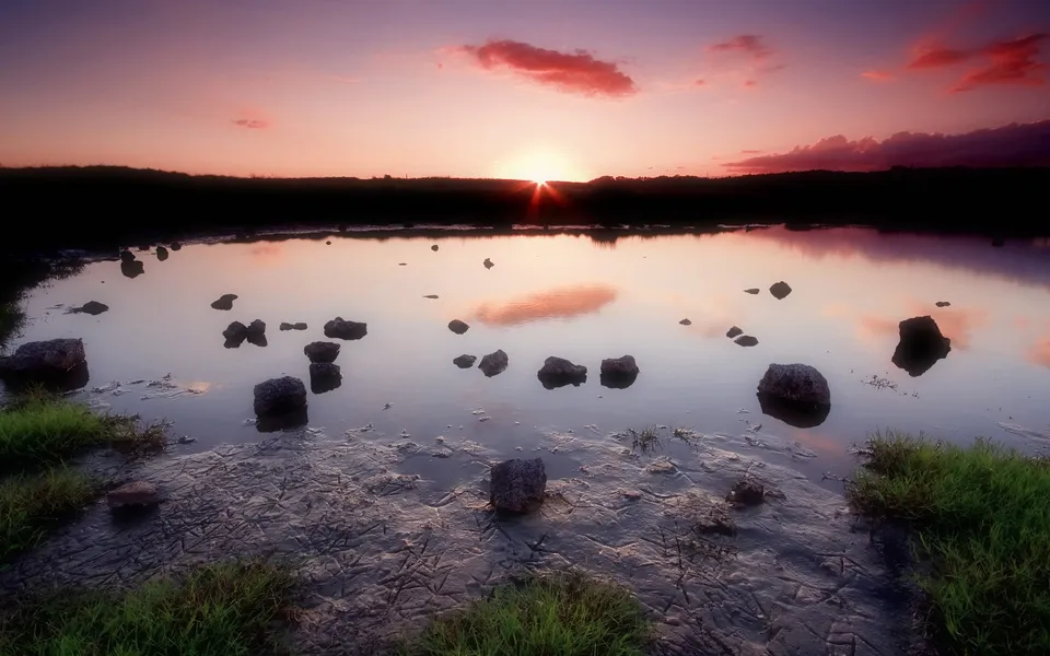A soft pink and purple sunset over still water with scattered rocks.