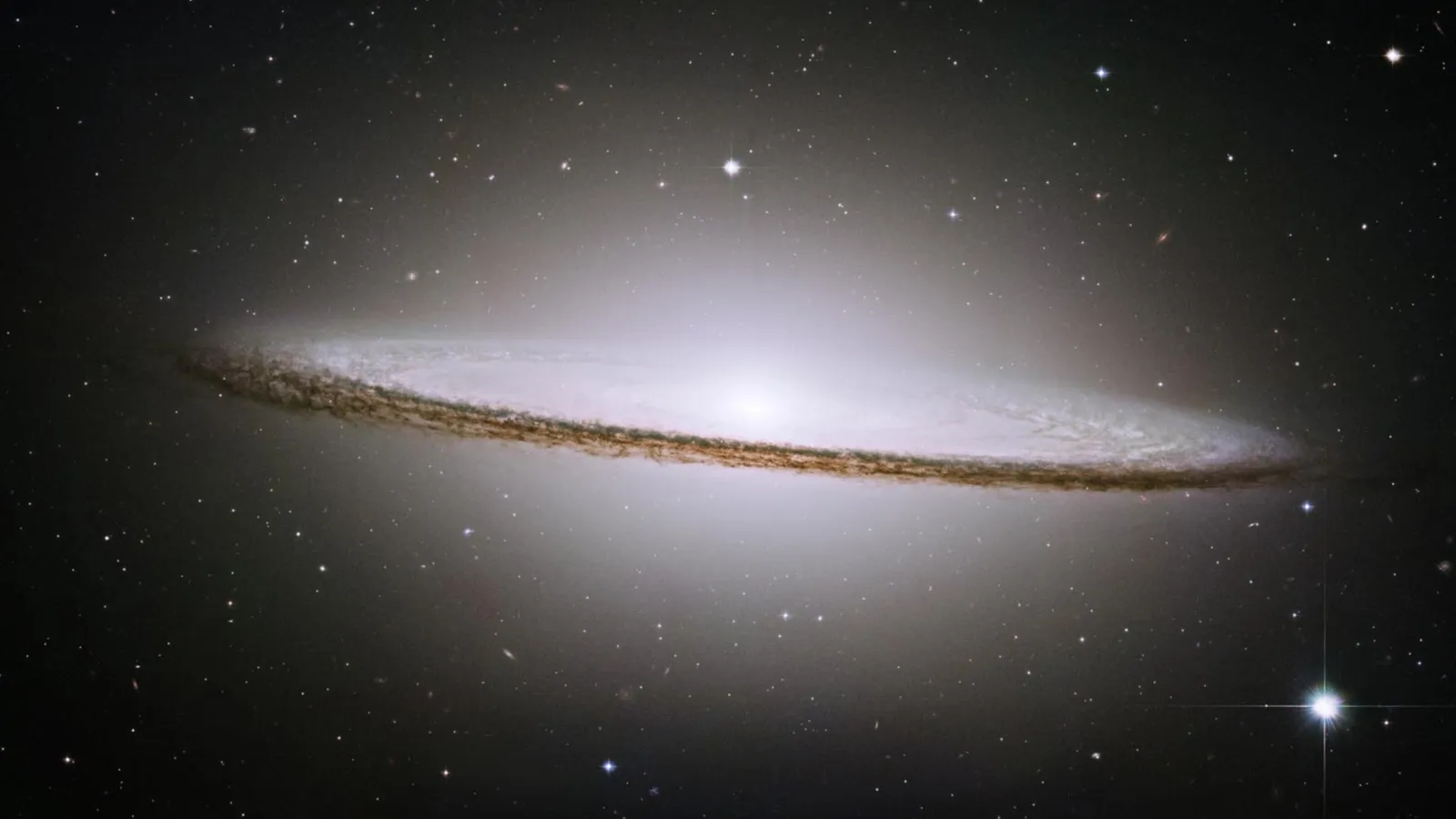 A spiral galaxy viewed edge-on, with a prominent dust lane and bright central bulge, surrounded by stars.