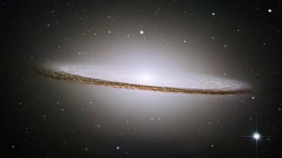 A spiral galaxy viewed edge-on, with a prominent dust lane and bright central bulge, surrounded by stars.