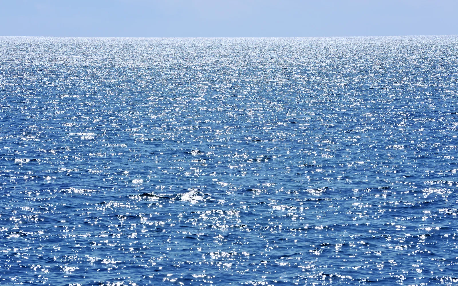The vast blue ocean surface is covered in countless sparkling reflections of sunlight.