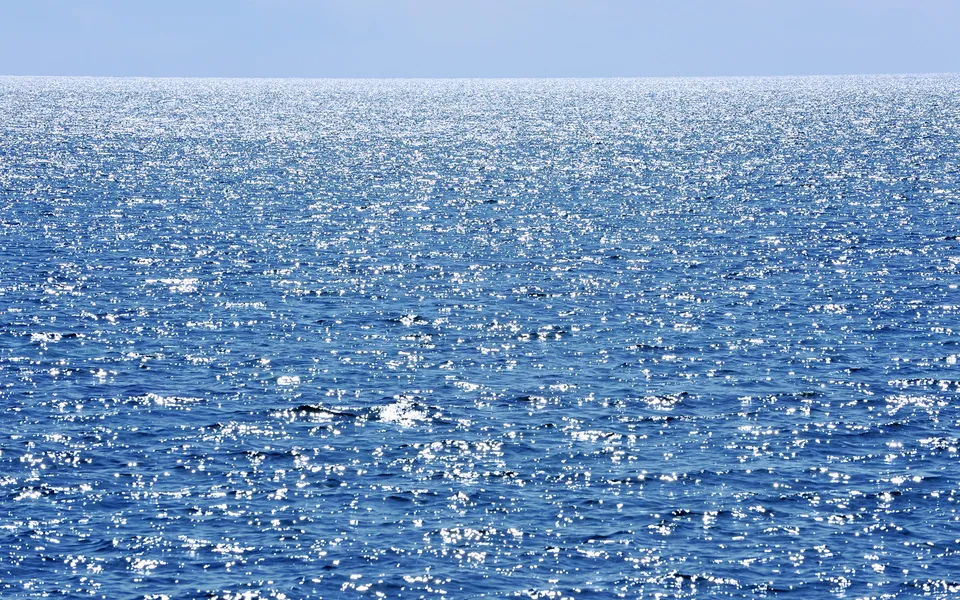 The vast blue ocean surface is covered in countless sparkling reflections of sunlight.