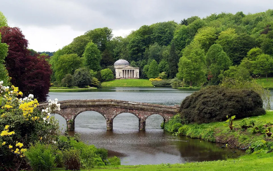 A picturesque landscape featuring a stone bridge over a lake, with a classical temple on a hill in the background.