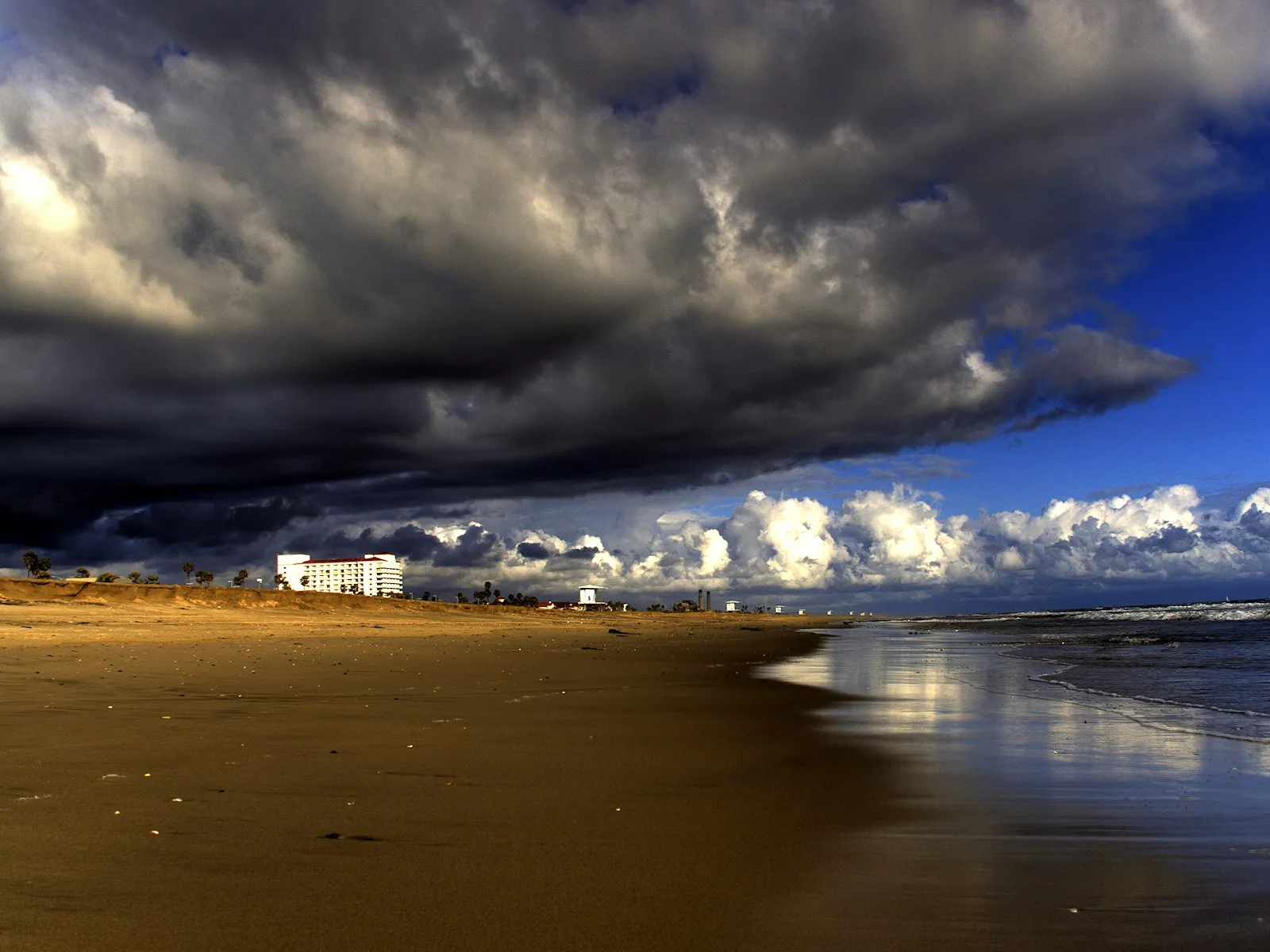 A wide sandy beach with dark storm clouds gathering overhead and the ocean on the right.