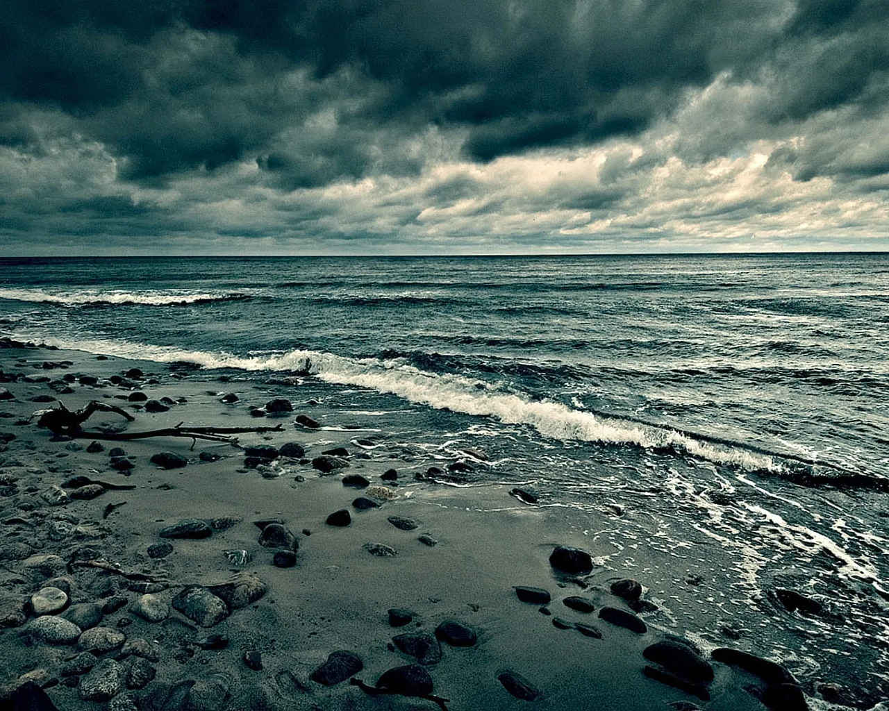 A dark, stormy sky looms over a rocky beach with waves crashing ashore.