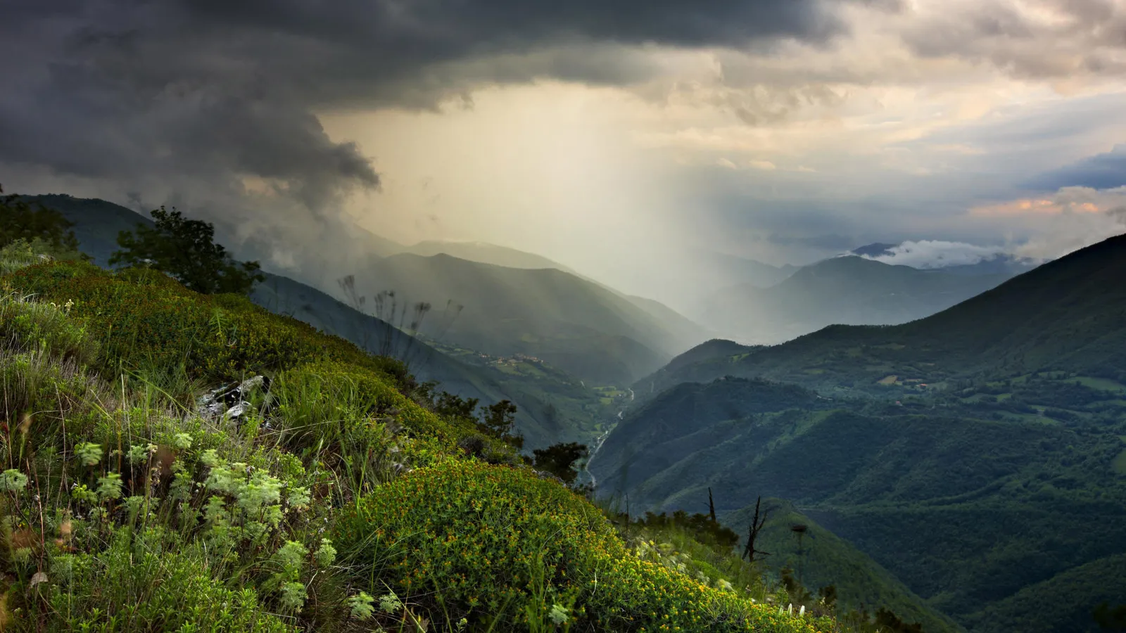A dramatic view of a mountain valley with sunbeams breaking through dark storm clouds.