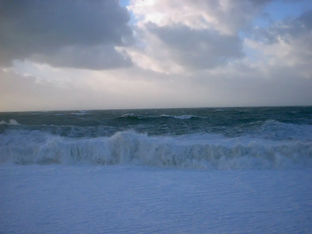 Large waves crash onto a beach under a dramatic, cloudy sky.