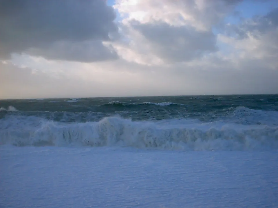Large waves crash onto a beach under a dramatic, cloudy sky.