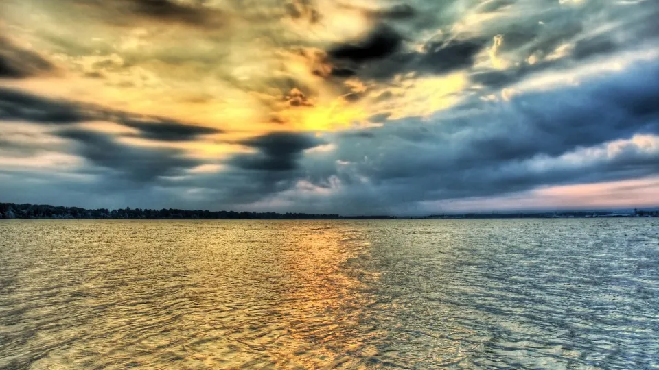 A dramatic sky with dark clouds and golden light over a calm body of water.