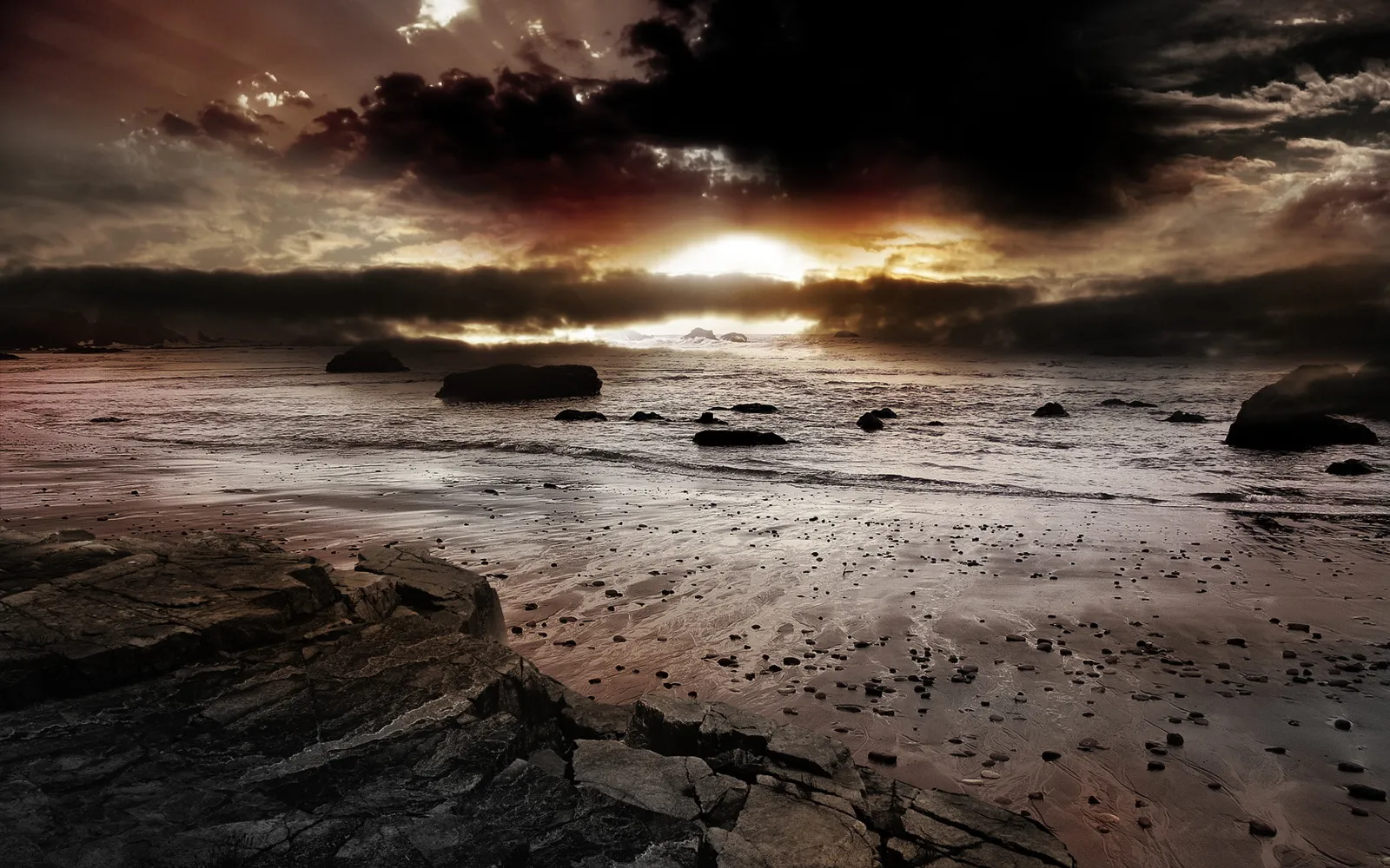 Dramatic sunset with sun breaking through dark clouds over a rocky beach and ocean.