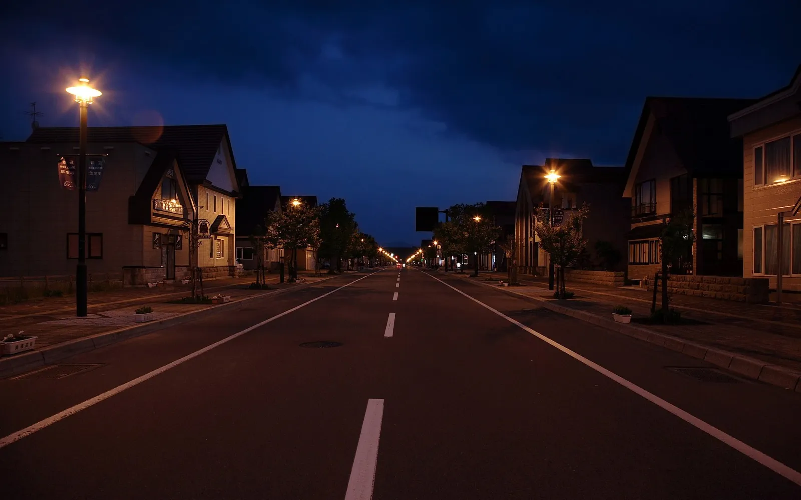 A straight road lined with houses and streetlights at dusk.