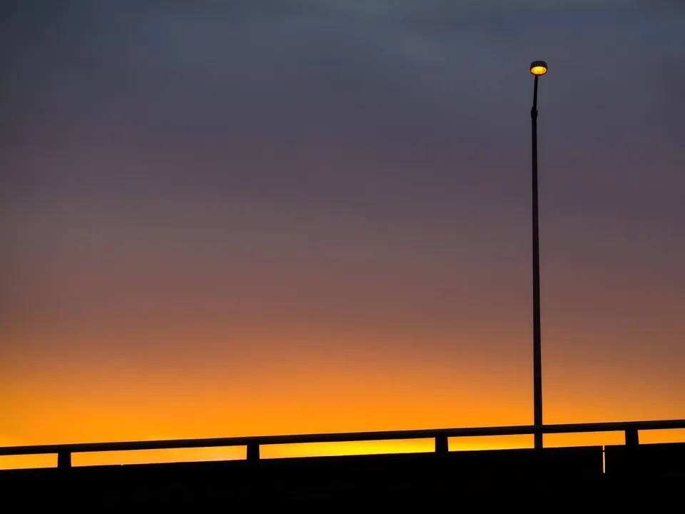 A single streetlight glows orange against a gradient sky of purple and orange, silhouetting a bridge railing.