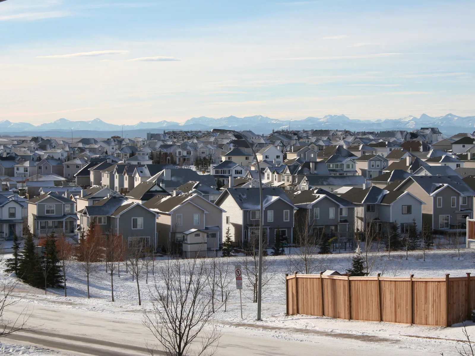 A wide view of a suburban neighborhood covered in snow, with mountains in the distance under a clear blue sky.