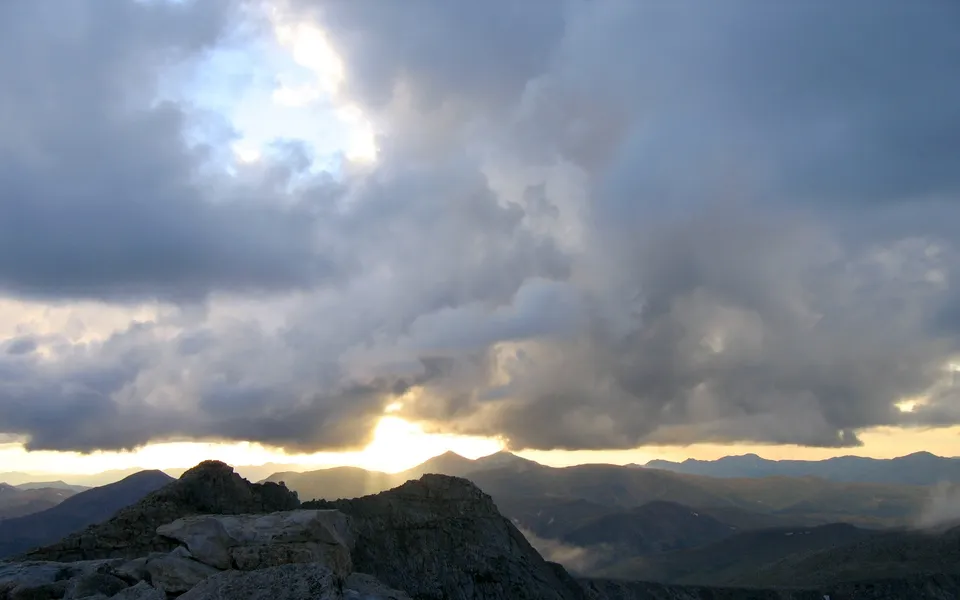 Sunlight streams through dark clouds over rugged mountain peaks.