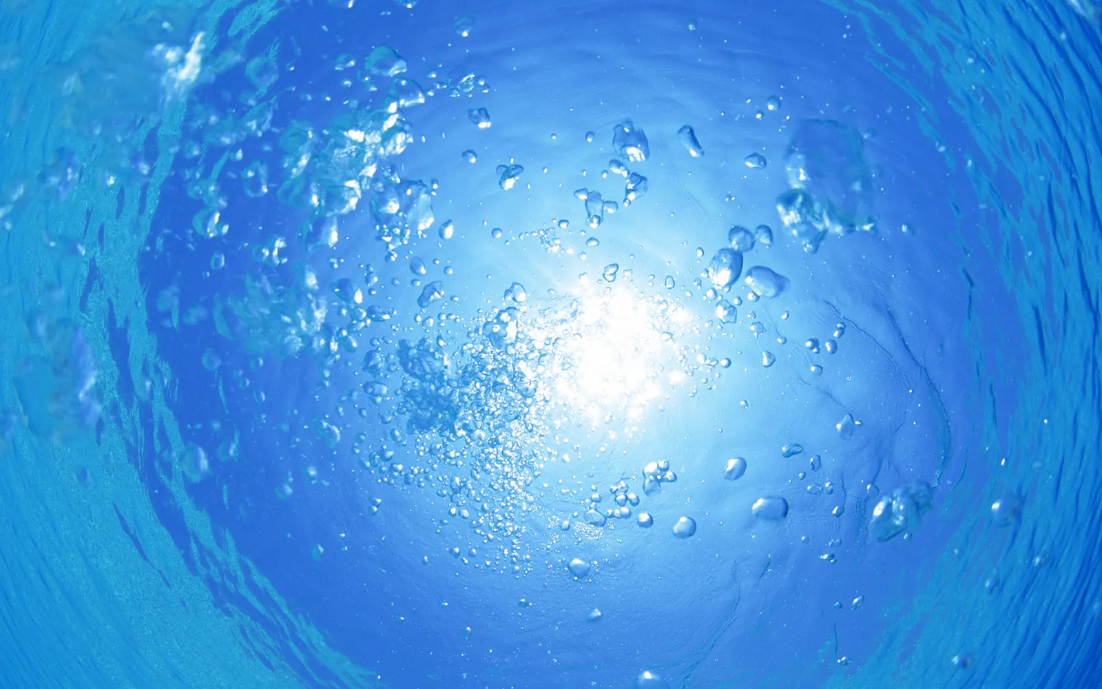 Sunlight streams through sparse underwater bubbles, creating an ethereal glow against the deep blue water.