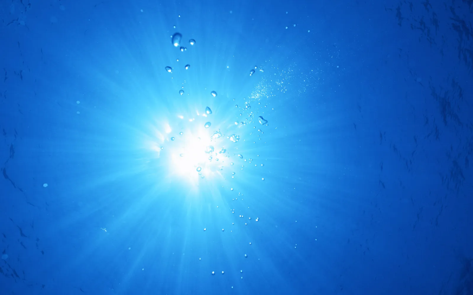 Underwater view of sunbeams radiating through the blue ocean water with rising air bubbles.