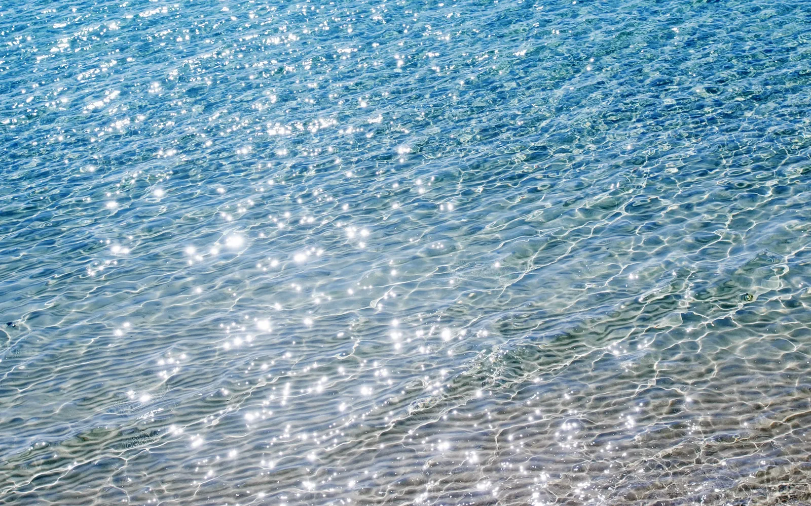 Close-up view of clear blue ocean water with sunlight sparkling on the surface and ripples creating patterns.