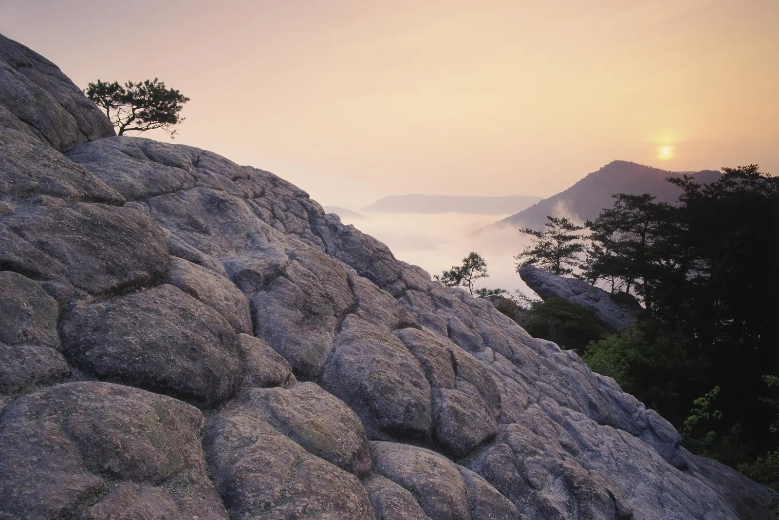 A rocky foreground leads to misty valleys and mountains at sunrise.