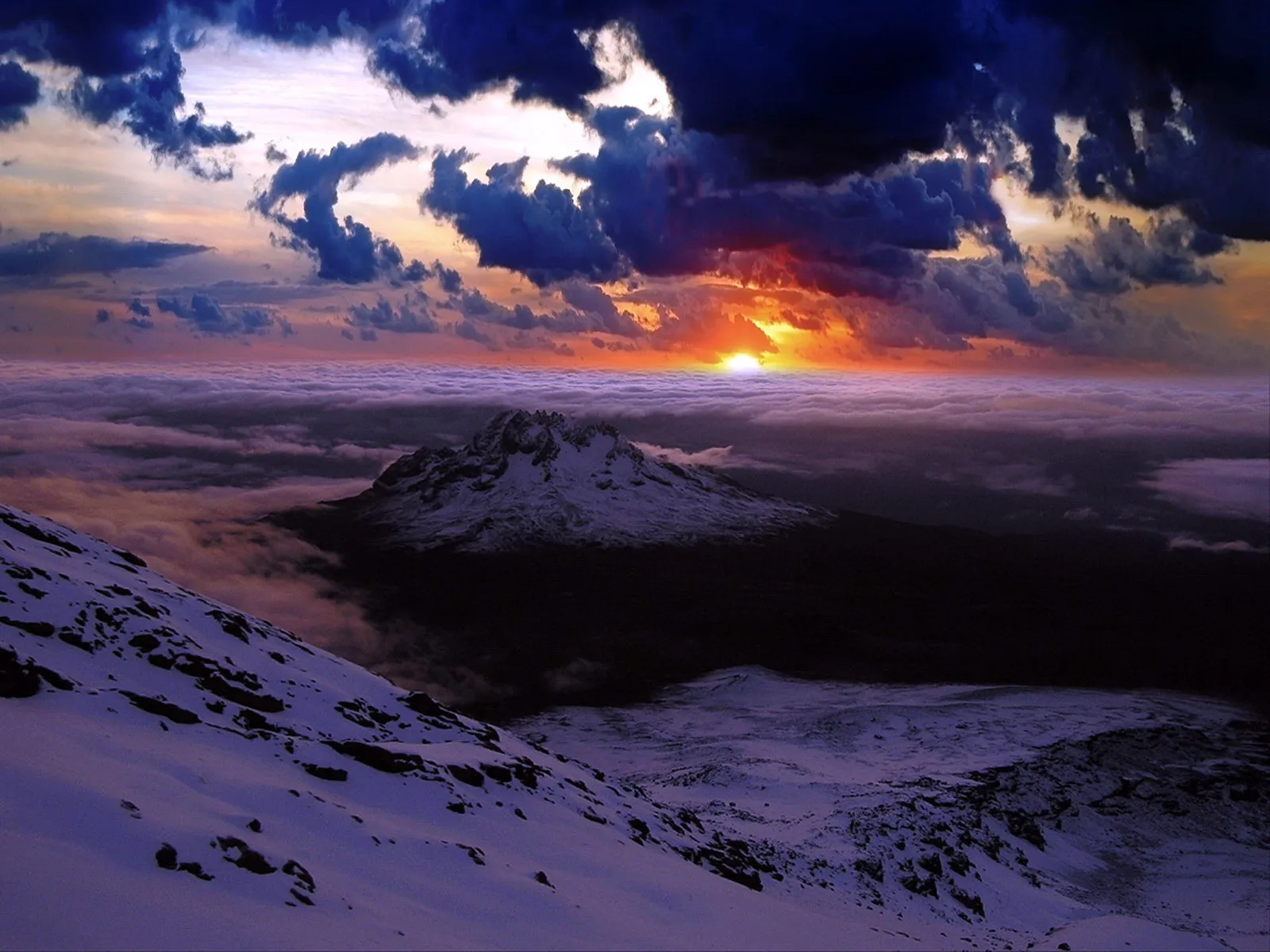 A vibrant sunrise illuminates dark clouds above a snow-covered mountain peak emerging from a sea of clouds.