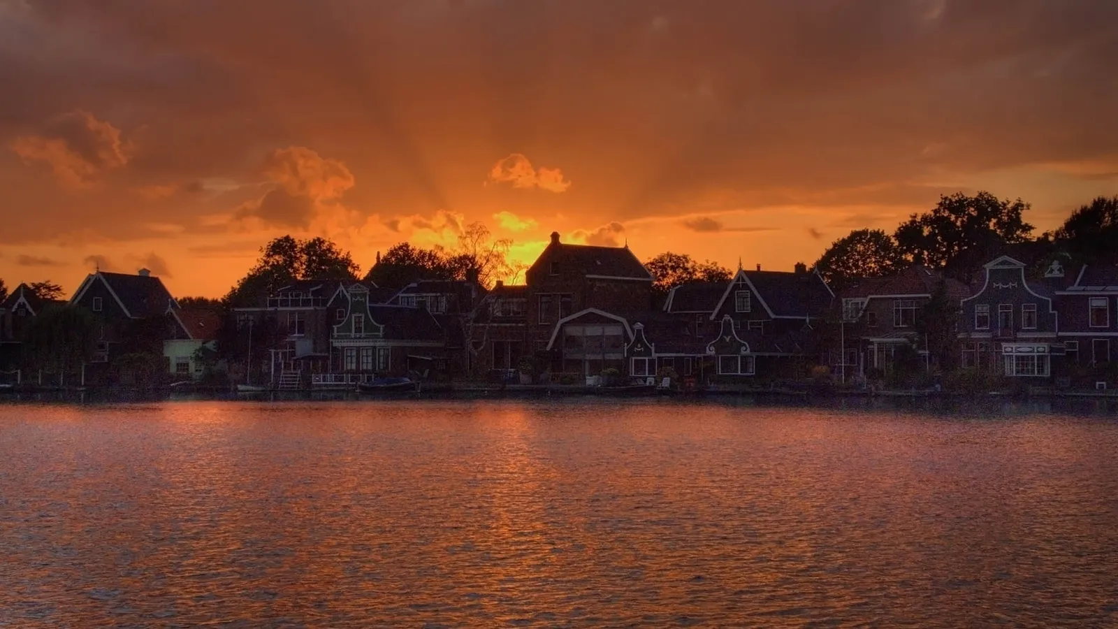 A vibrant sunset casts an orange glow over traditional canal houses and a reflective body of water.