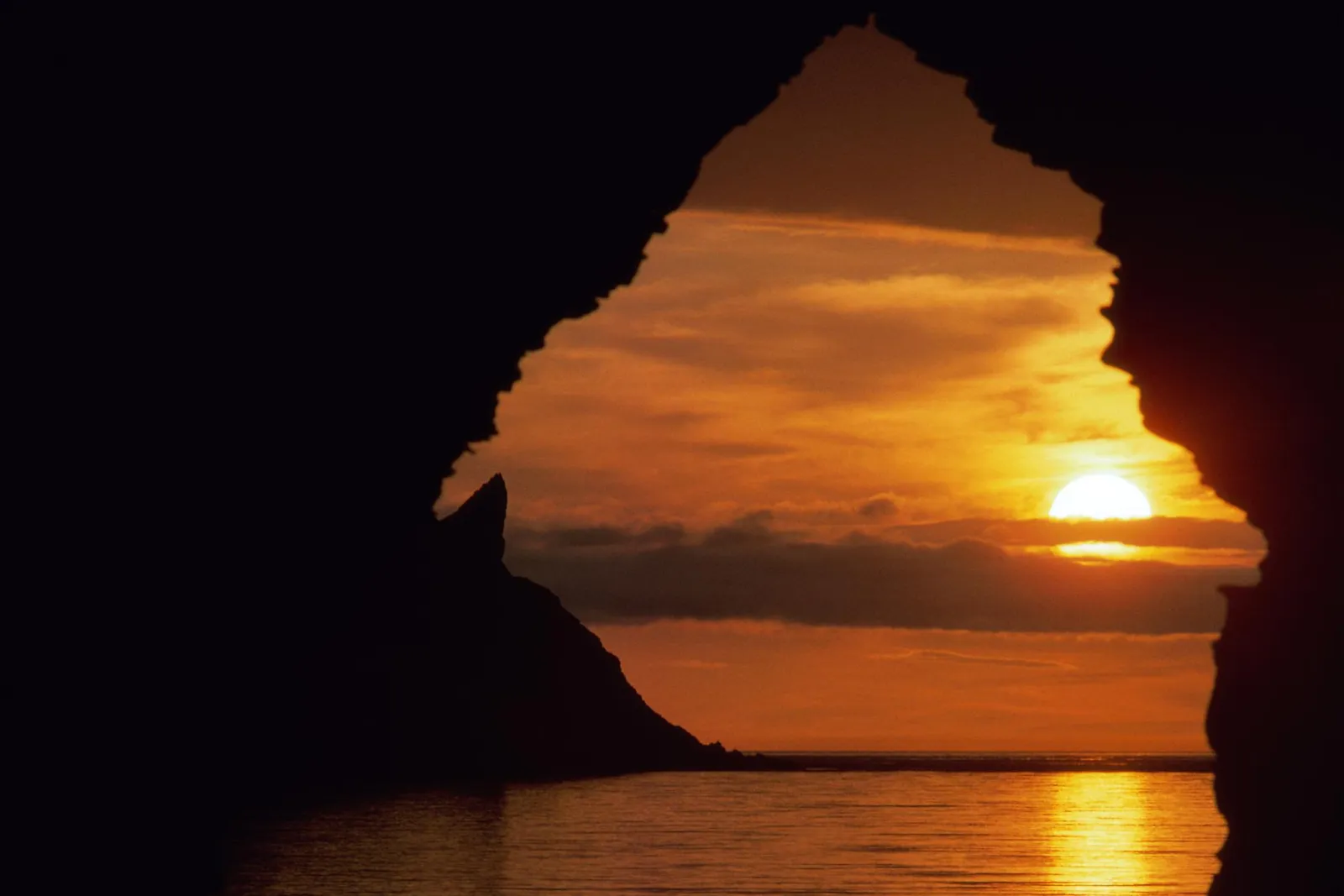 View of a vibrant sunset over the ocean through a dark cave opening.