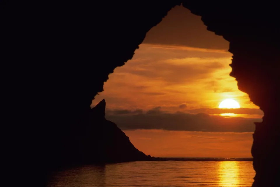 View of a vibrant sunset over the ocean through a dark cave opening.